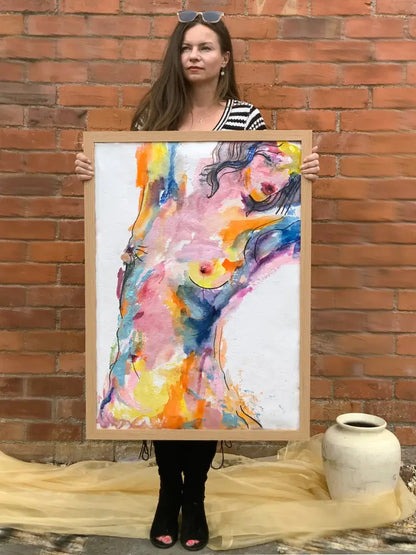 Woman holding a colorful abstract painting against a brick wall.