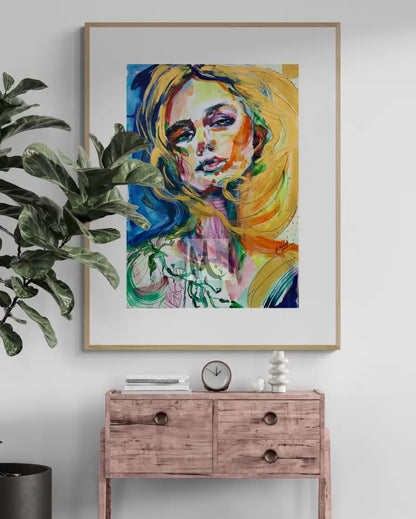 Framed abstract art of a woman's face on a wall above a wooden console table with decorative items.