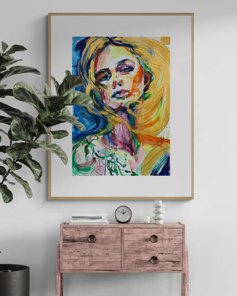 Framed abstract art of a woman's face on a wall above a wooden console table with decorative items.