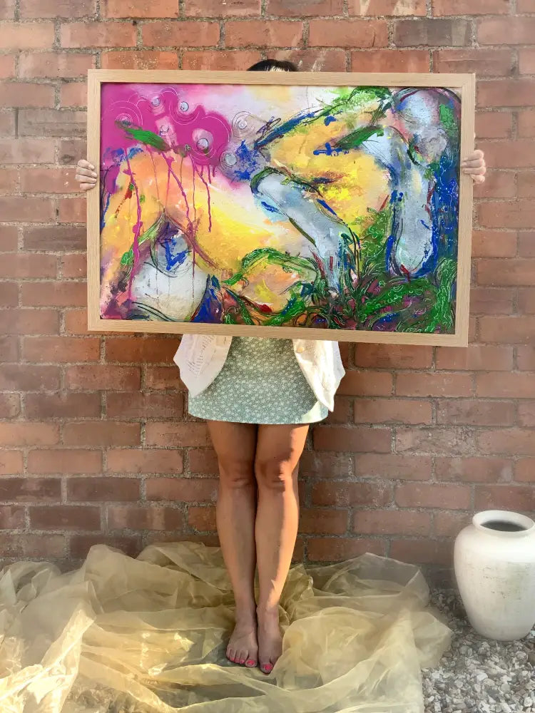 Person holding a colorful abstract painting against a brick wall.