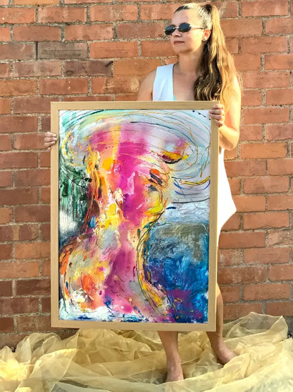 Woman holding a large abstract painting of a woman against a brick wall.